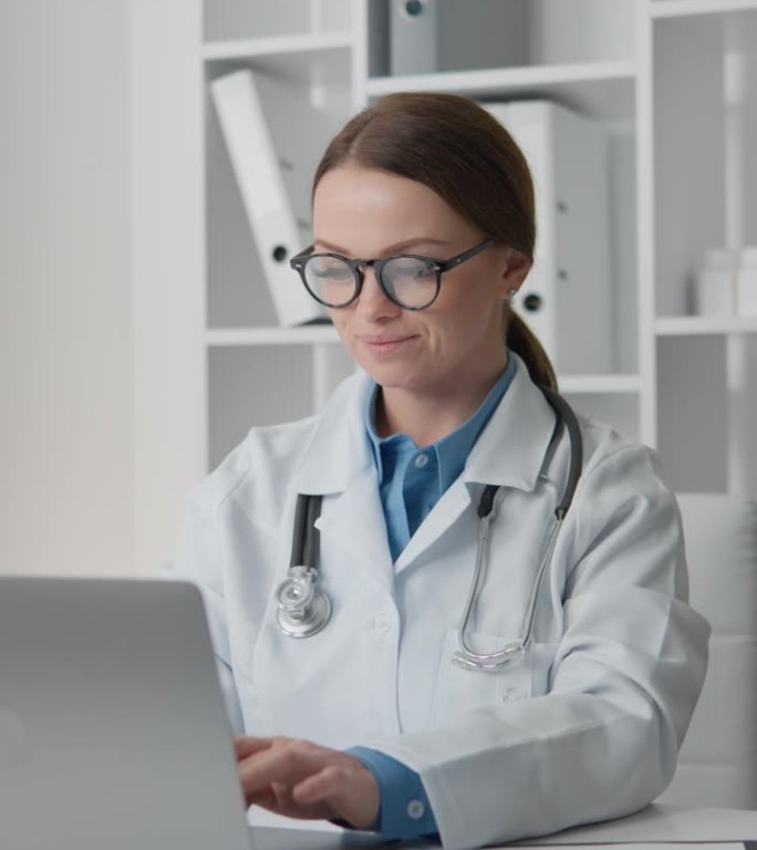 带听诊器工作的女医生专注于笔记本电脑，分析医疗数据，为每位患者制定个性化的治疗方案。穿白大褂戴眼镜的