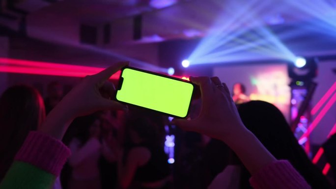 一个女孩横着拿着绿色屏幕的智能手机拍摄