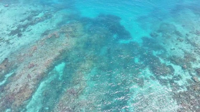 清澈的绿松石水露出水下礁石。阳光在海面上闪烁。空中俯视无人机视图