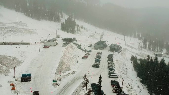 无人机在覆盖着树木、小屋和停着的汽车的雪山上空飞行