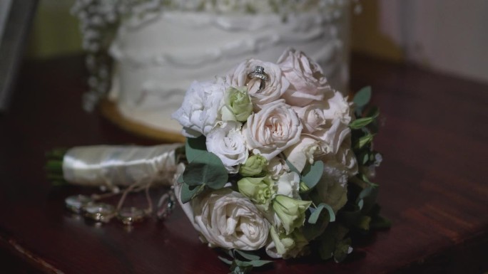 闪亮的白金结婚戒指镶嵌在新娘捧花的玫瑰花瓣中间。婚礼的细节