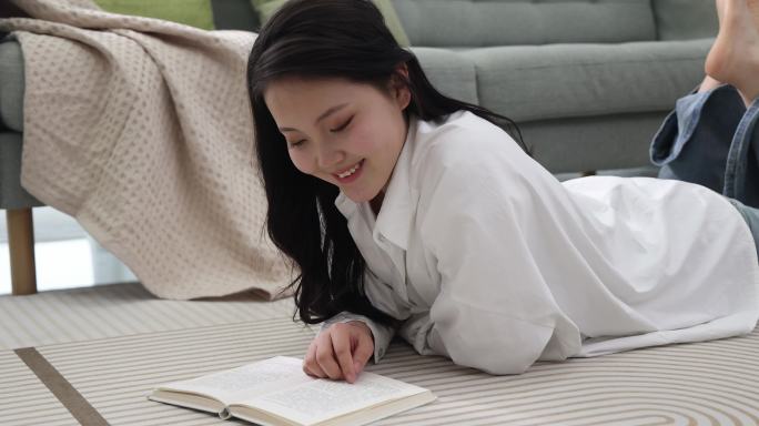 一位年轻女士趴在地毯上看书