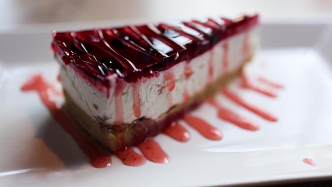 这段视频展示了一个颓废的芝士蛋糕，上面装饰着一层光滑的红色果冻。奶油芝士蛋糕与充满活力、光泽的覆盆子
