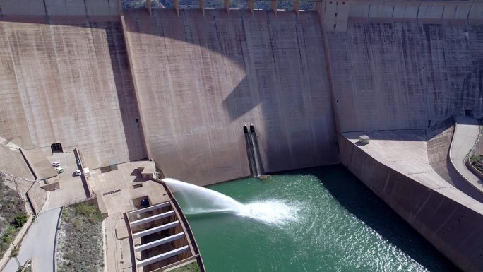 重力坝放水。豪厄尔饥饿阀工作。下降鸟瞰图在大坝和河流。可再生能源。水电站。到站
