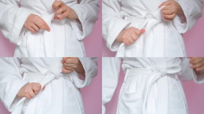 年轻女子在浴袍上系上带子，粉色背景特写。