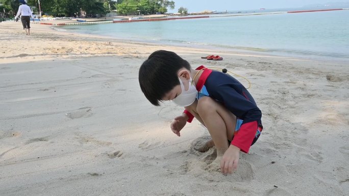 慢动作场景快乐的男孩在沙滩上玩得开心，孩子戴上covid - 19口罩