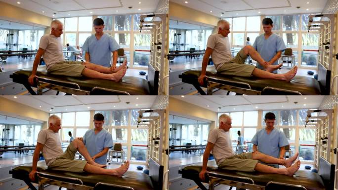 男治疗师在物理治疗期间帮助一位老年男性病人弯曲他的腿