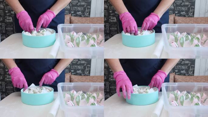 一位妇女把自制的棉花糖放进盒子里。这个盒子是蓝绿色的。旁边的桌子上有西风郁金香