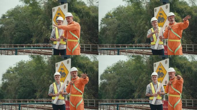 高级铁路专业工程师头戴钢盔，身穿橙色防护服，向拿着铁路轨道施工图的初级同事讲解铁路轨道的主要组成部分