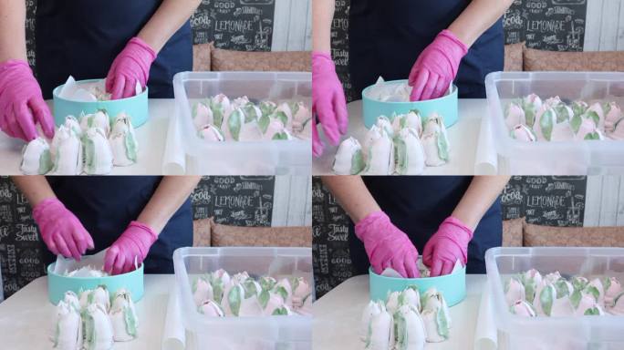 一位妇女把自制的棉花糖放进盒子里。这个盒子是蓝绿色的。旁边的桌子上有西风郁金香。