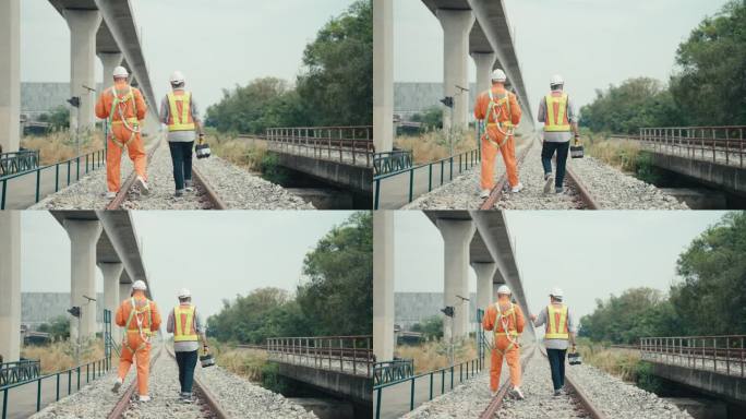 两名美国成年高级铁路工程师，头戴安全帽，身穿防护服，在铁路轨道上行走，在车辆段观察两条轨道的规定距离