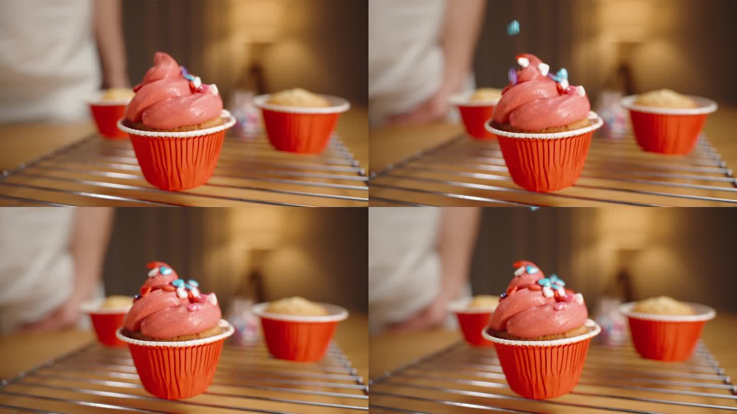 糕点师把糖屑撒成五颜六色的心状，撒在红糖霜的纸杯蛋糕上。慢镜头，特写。