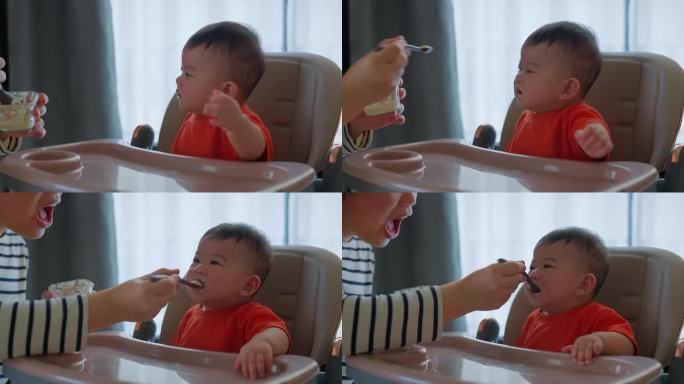 亚洲家庭生活。年轻的妈妈用勺子喂婴儿，坐在客厅的高脚椅上，饭又脏又乱的亚洲妈妈试着喂第一顿饭