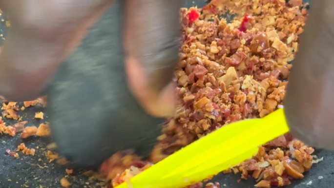 一位家庭厨师用研钵和杵把花生和辣椒磨成沙茶酱，用于传统的印尼烹饪