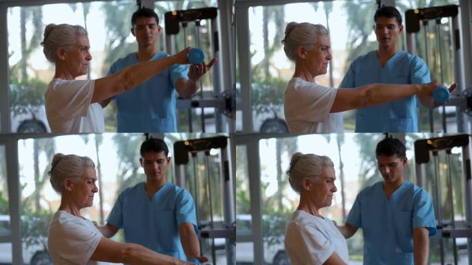 男治疗师在物理治疗期间帮助一位专注的老年妇女用哑铃锻炼手臂