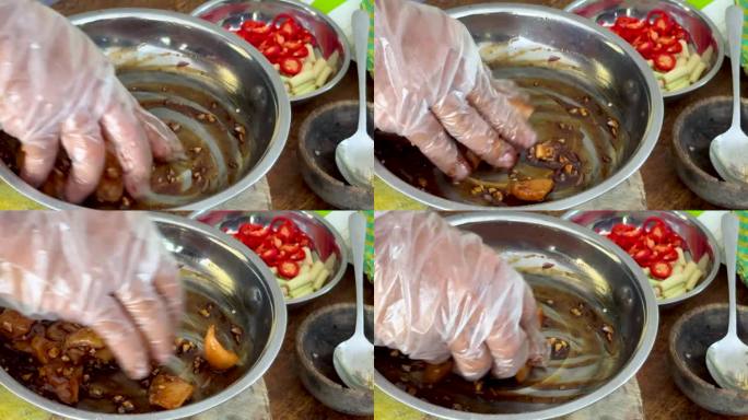 一名厨师用戴着手套的手将酱油、香料和调味料混合到生鸡肉中，同时烹饪传统的巴厘岛沙茶鸡肉串。