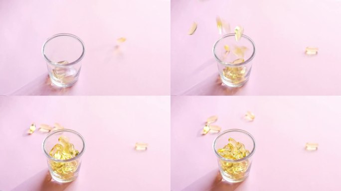 含有维生素的透明黄色胶囊被倒入粉红色背景的透明玻璃杯中。鱼油补充剂。健康、维生素和药物的概念。欧米茄