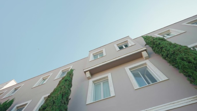 意大利住宅建筑的传统立面景观，长矩形窗户，没有阳台，装饰着常绿白色雪松的高柱，背景是清澈的蓝天