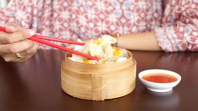 一位妇女正在用红筷子吃蘸着酱汁的点心饺子