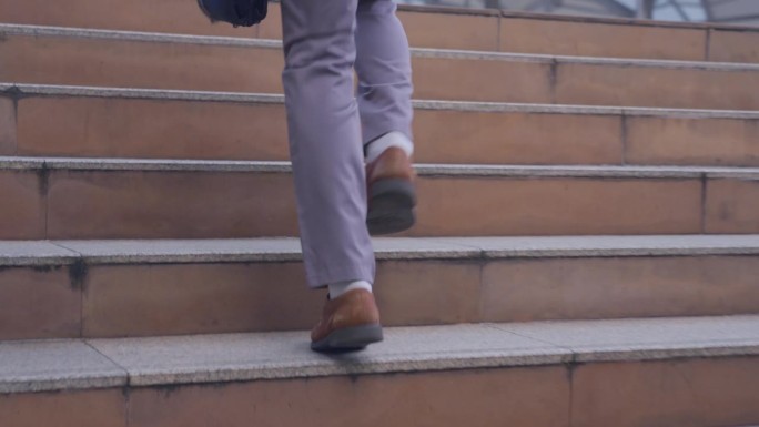 匆忙的亚洲年轻商人在办公室跑上楼梯去上班的特写镜头。上班族手持商务手袋，穿着办公室正装，走在城市的户