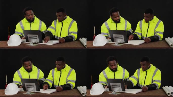 穿着反光绿色制服的黑人工程师坐在桌子上，手里拿着蓝图。