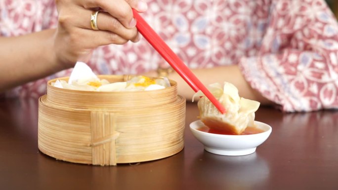 一位妇女正在用红筷子吃蘸着酱汁的点心饺子
