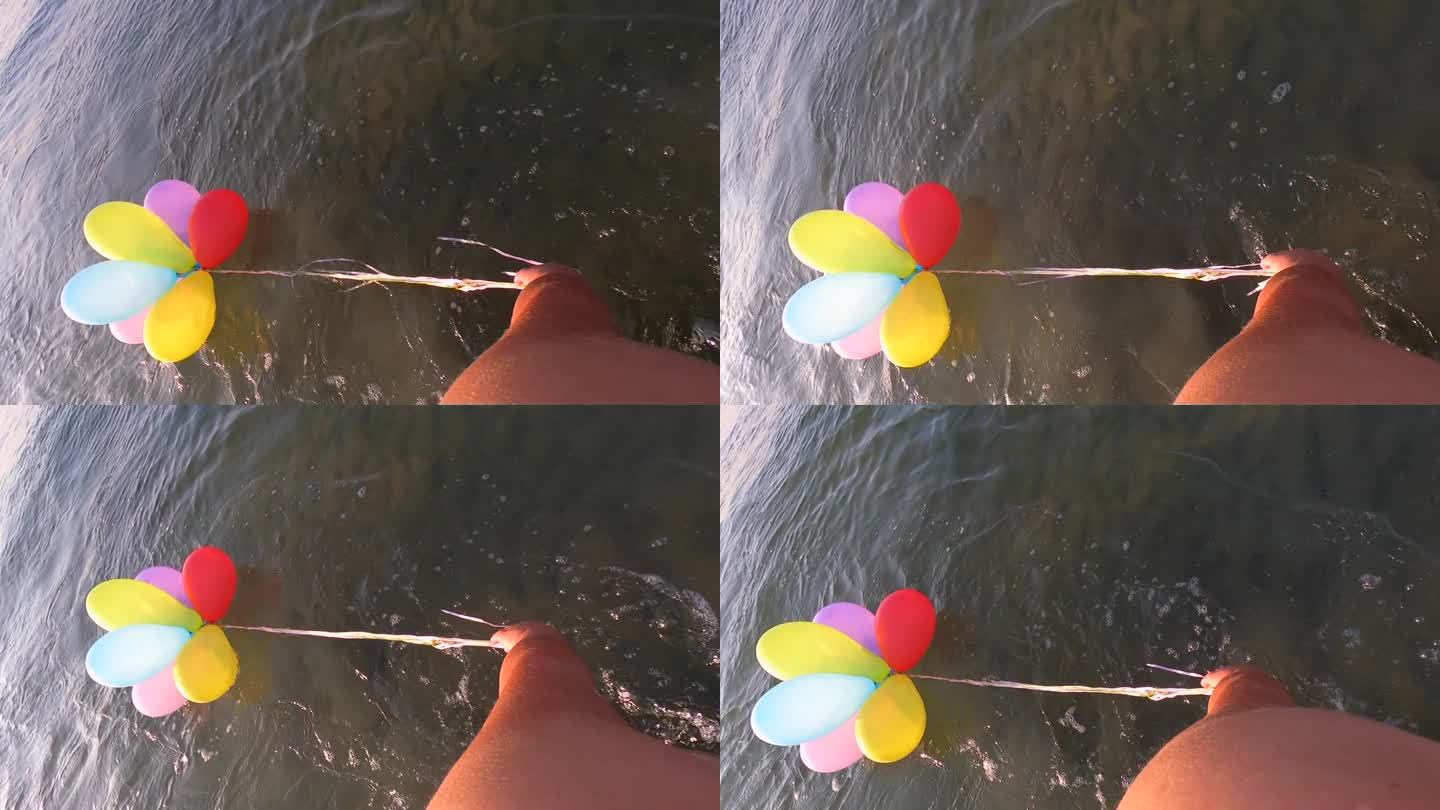 在一个阳光明媚的早晨，一个人拉着一束彩色的小气球，用丝带绑在水面上。慢动作