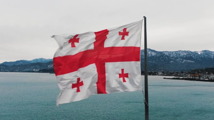 在大海和山脉的背景下，格鲁吉亚的大国旗在风中飘扬，鸟瞰图