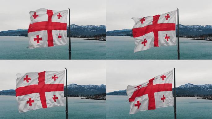 在大海和山脉的背景下，格鲁吉亚的大国旗在风中飘扬，鸟瞰图