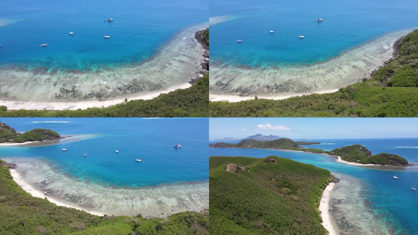 天堂海滩的电影鸟瞰图，清澈的海浪冲击着海岸。船只漂浮在碧绿的水面上，直到露出整个岛屿和雄伟的山脉(斐