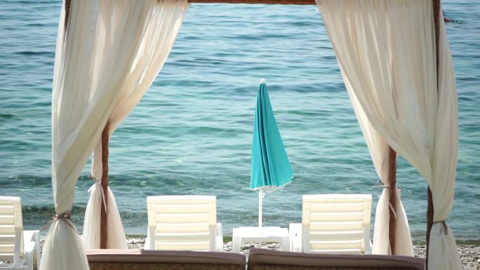 平房。沙滩休闲床与白色丝绸窗帘。海边带篷的空躺椅床。沙滩椅和遮阳伞。避暑度假的概念。没有人。慢动作