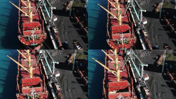 一辆港口起重机卸下一艘装有肥料的船舶，并将肥料倒入铁路车厢，鸟瞰图