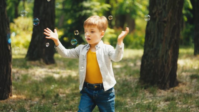 小男孩在公园里专心抓肥皂泡，周末快乐