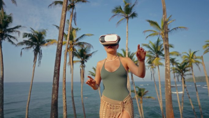 女人带着VR头盔探索热带天堂，在真实的棕榈树中感受虚拟海风。享受身临其境的科技，在海边放松。，触摸虚