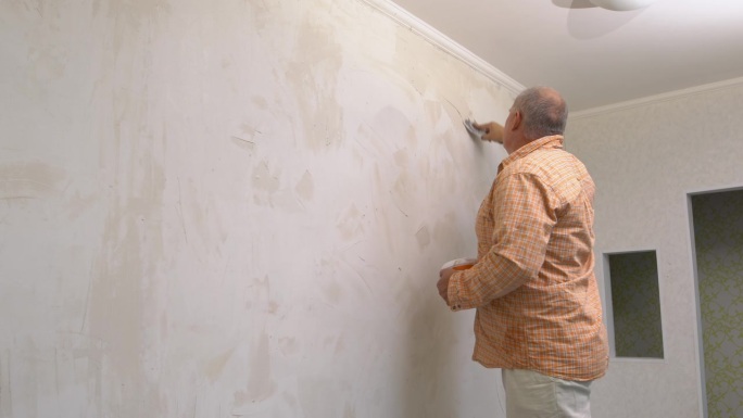 一个人把腻子涂在墙上，用抹刀把腻子抹平。