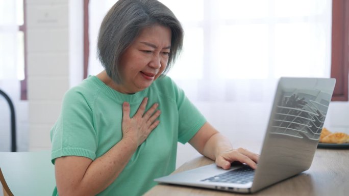 忧心忡忡的老年女性在使用笔记本电脑时感到不适，疼痛打断了她的注意力