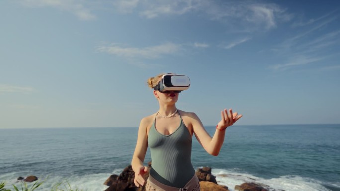 戴着VR头盔的女人探索虚拟空间，用手势导航游戏或虚拟世界。海边背景，互动科技，身临其境的体验。穿着便