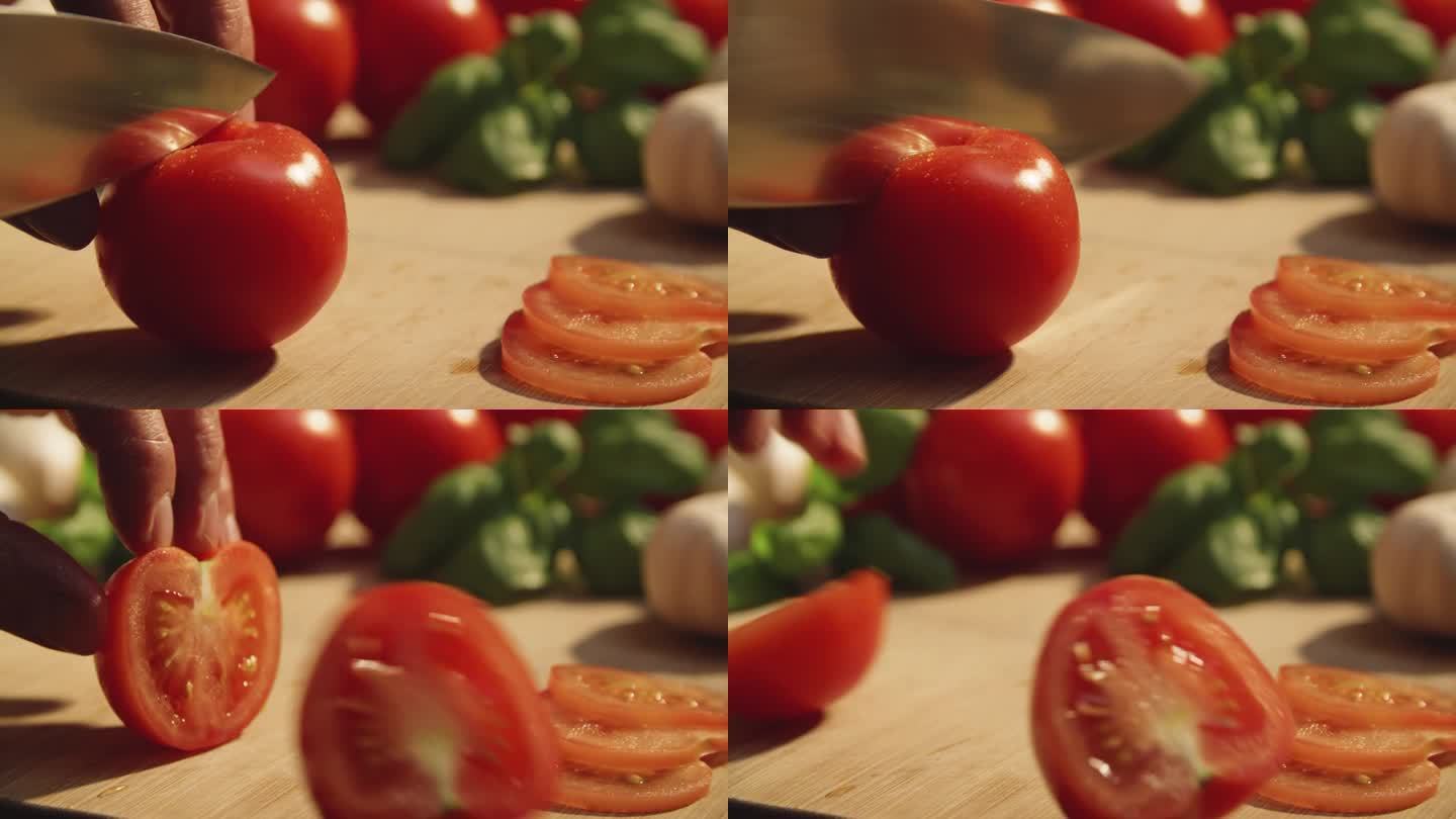 厨师用刀沿着指尖将番茄切成两半的特写。特写镜头锋利的刀切番茄之前模糊的背景在健康的意大利厨房设置。