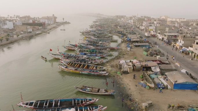 空中摇上。色彩斑斓的独木舟停泊在被污染的塞内加尔河上。塑料污染，塞内加尔圣路易，联合国教科文组织世界