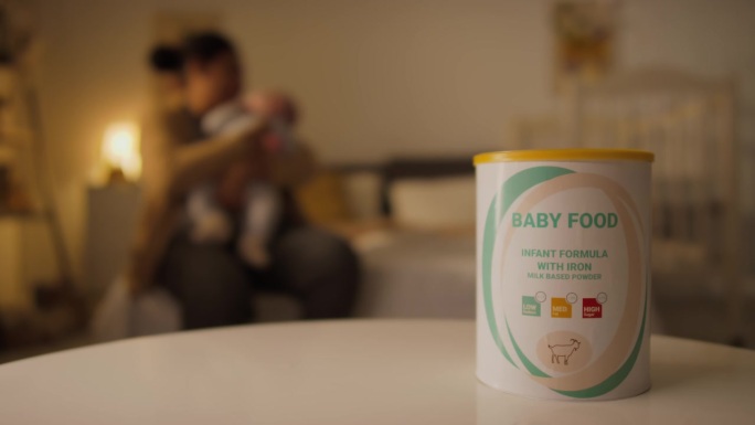 卧室桌上放着一罐婴儿配方奶粉，一位不知名的母亲抱着婴儿
