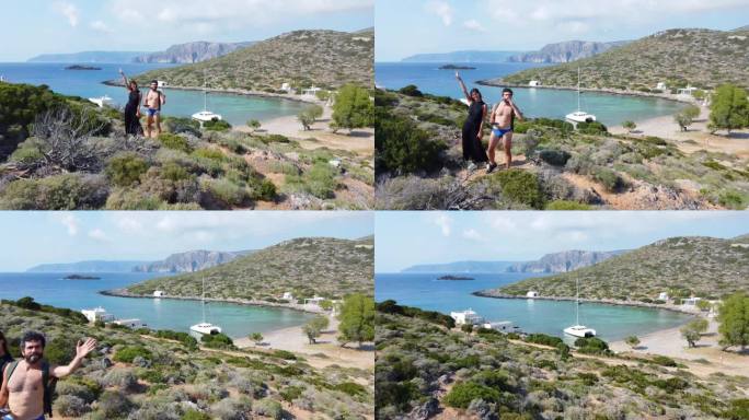 一名身穿黑色连衣裙的女子和一名身穿泳装的男子对着镜头挥手，欣赏着希腊一个有白色房屋和帆船的隐蔽海湾的