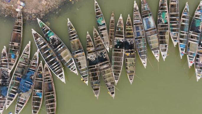 空中特写镜头直接向下平移。色彩斑斓的独木舟停泊在被污染的塞内加尔河上。塑料污染，塞内加尔圣路易，联合
