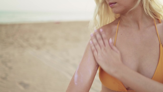 暑假期间，一名穿着比基尼的年轻女子在海滩上涂防晒霜。皮肤护理，防止太阳辐射