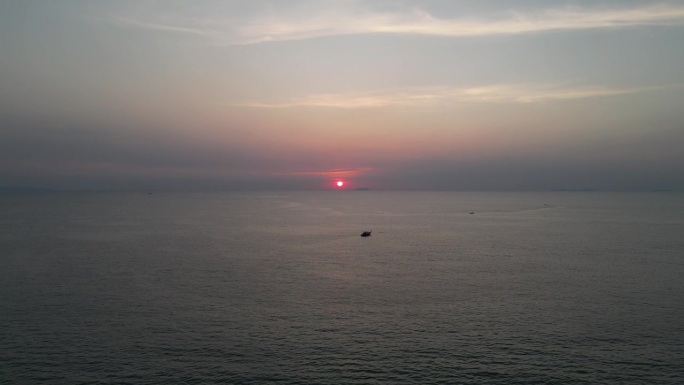 远处夕阳西下，平静的海面上的船只。无人机拍摄的水上日落鸟瞰图。红色的太阳即将沉入水面，小岛在地平线上