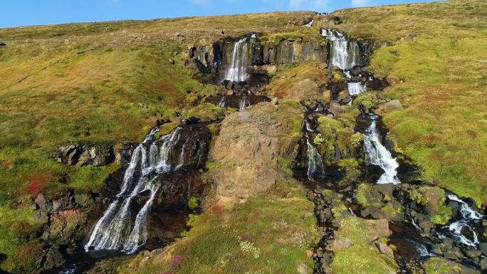 从山顶流下的水流形成许多小瀑布的令人惊叹的景色。这张照片是在一个晴朗的晴天拍摄的。山上有棕色的土壤，