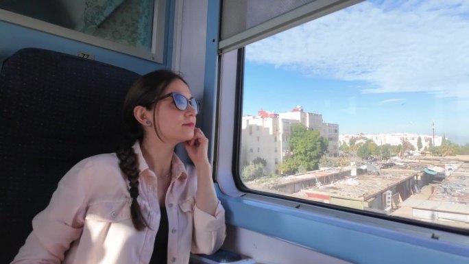 一位戴着墨镜的孤独的旅行者，从火车的窗口平静地望向窗外，欣赏着城市的风景。