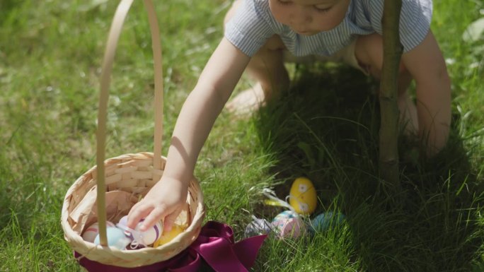 小孩子的手从户外的绿草地上捡起复活节彩蛋篮子