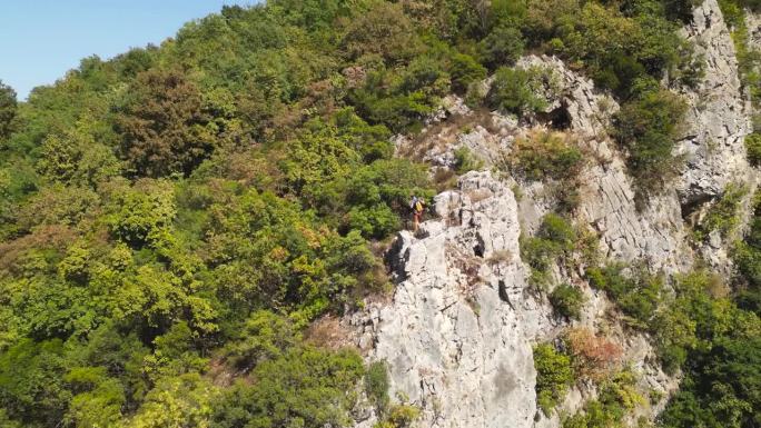 攀岩者到达攀岩岩石的顶端。登山者戴着红色的头盔和黄色的背包。