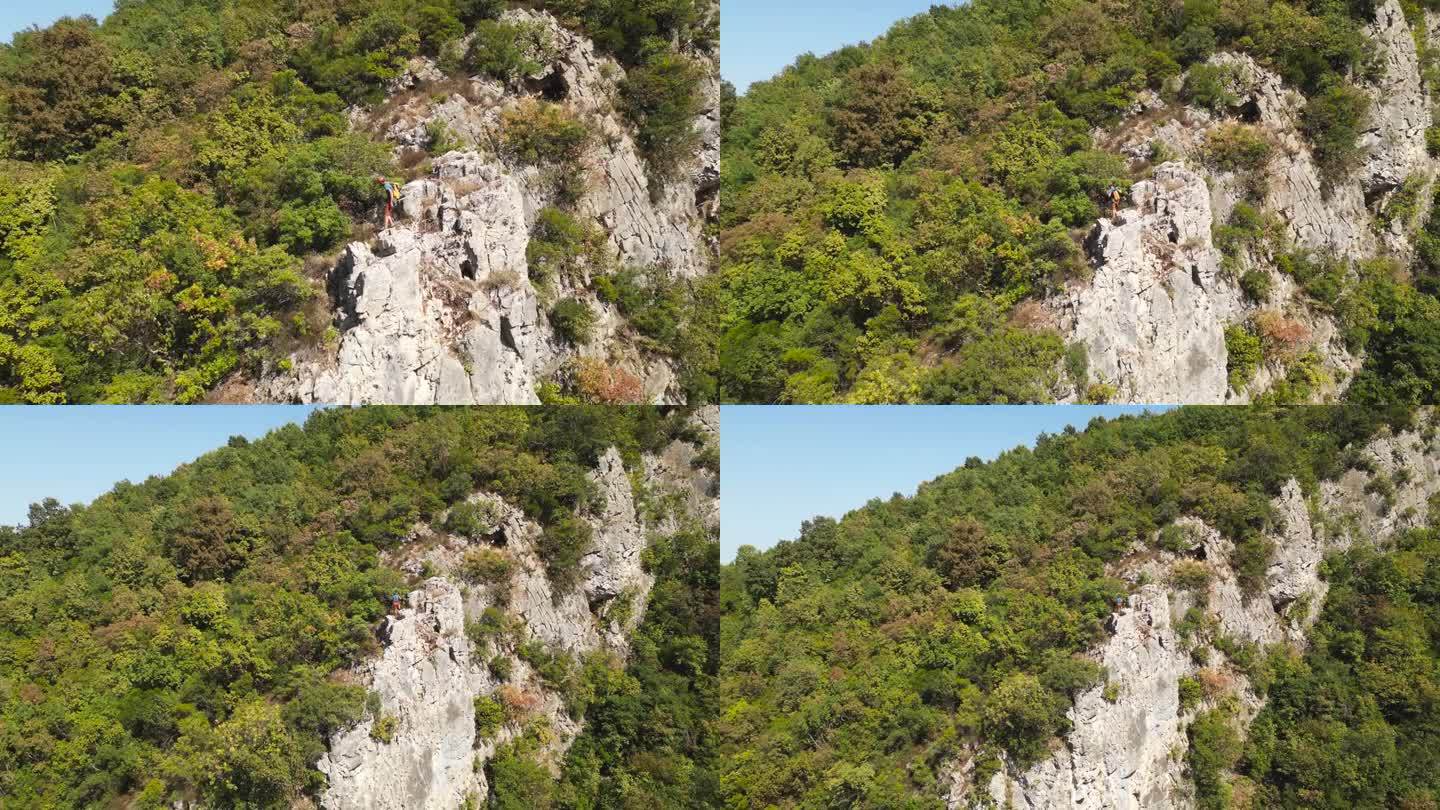 攀岩者到达攀岩岩石的顶端。登山者戴着红色的头盔和黄色的背包。