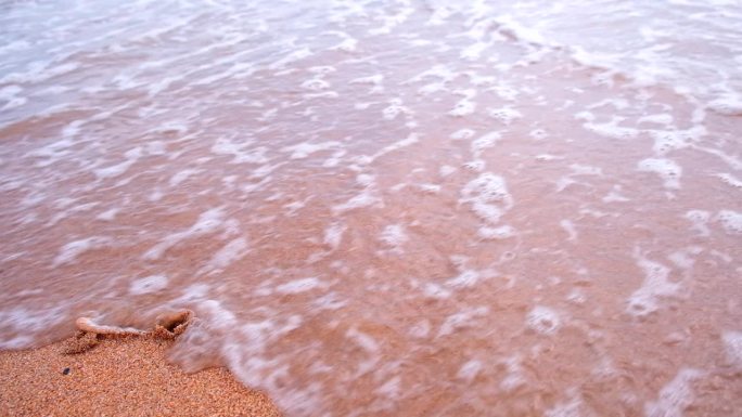 在海边的沙滩上手写的铭文，数字2024。2024年被海浪冲走的黄沙上的特写。缓慢的运动。年历和新年概